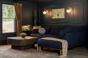 A dark-themed living room with a sofa, ottoman, coffee table, and two wall-mounted lamps. - Sauna, Hot Tub, Pet Friendly, Games - Hocking Hills (South Bloomingville)