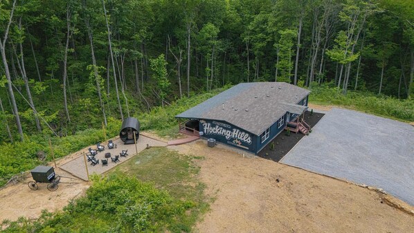 A cabin with a covered outdoor seating area, a fire pit, and a gravel path.