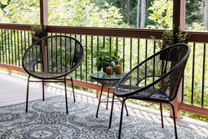 A balcony with two black wicker chairs, a small round table, and a potted plant.