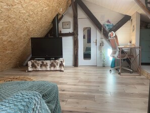 Une chambre située dans un espace de type « loft », avec un plafond en pente, un téléviseur posé sur un meuble, un bureau avec une chaise et un lit avec une couverture.