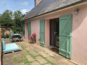 Une maison avec un patio, des volets verts, une porte et un petit jardin.