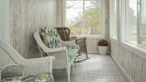A room with a rocking chair, a sofa, and a window with a view of trees and a house. - Heated Pool and Hot Tub near Downtown Lake Geneva! (Lake Geneva)