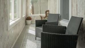 A sunlit room with wicker chairs, a potted plant, and a view through a window. - Heated Pool and Hot Tub near Downtown Lake Geneva! (Lake Geneva)