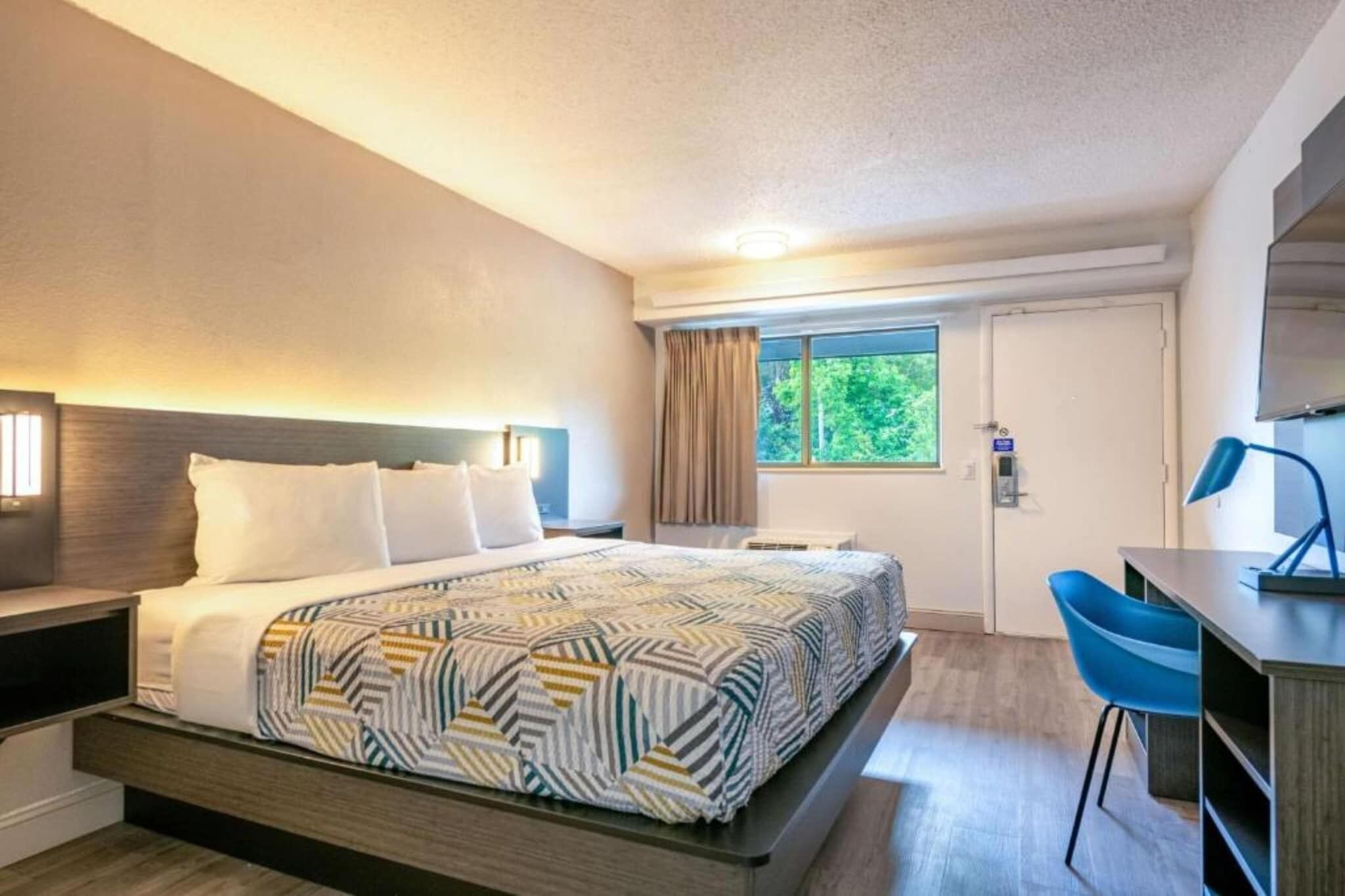 Ein Hotelzimmer mit Bett, Schreibtisch, Stuhl, Fenster und Tür.