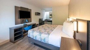 A hotel room with a bed, a desk, a chair, a TV, and a mirror.