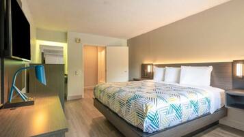 A hotel room with a bed, bedside table, lamp, and a view of the hallway.