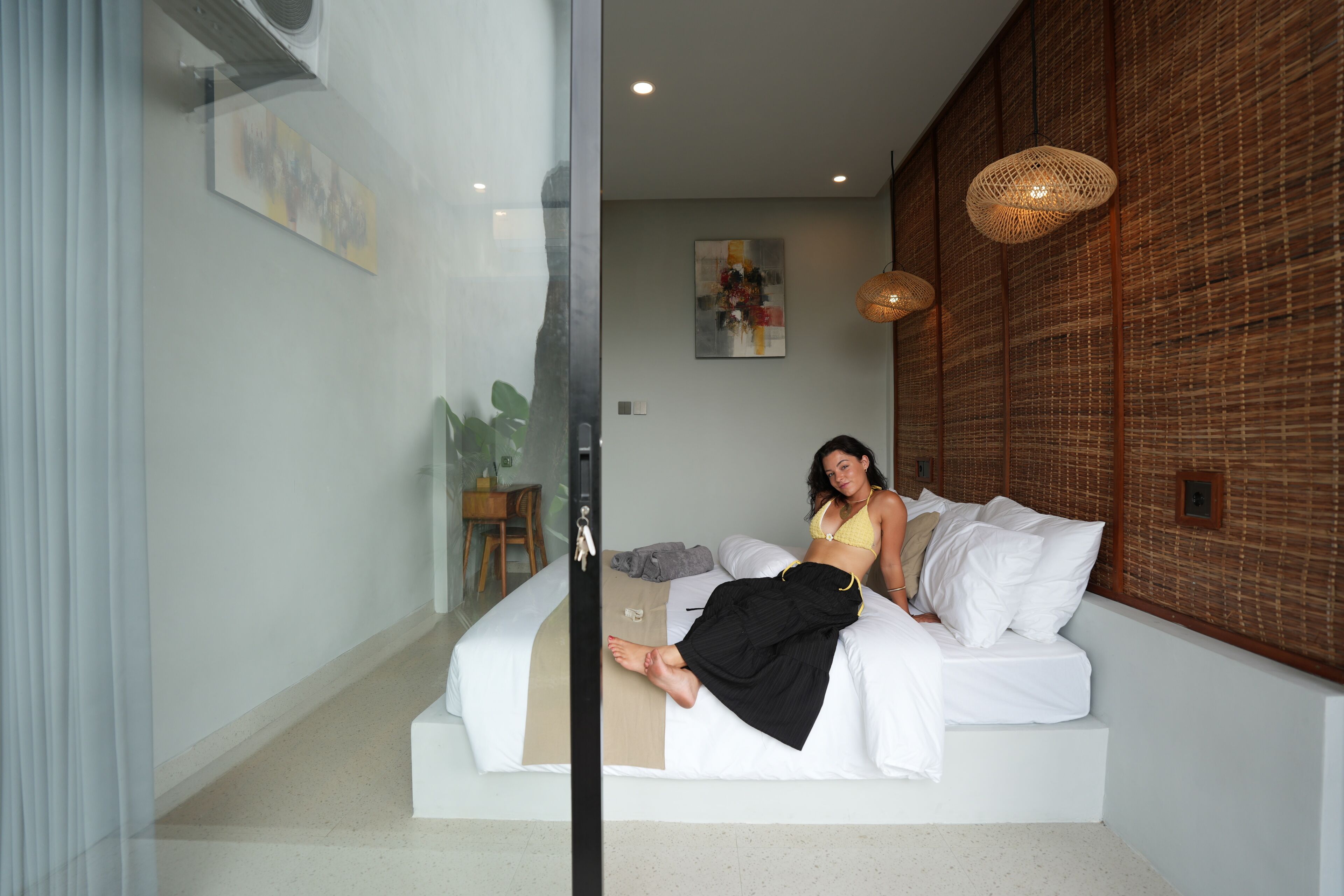 A modern bedroom with a bed, a glass partition, and a wall-mounted artwork.