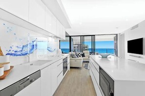 A modern kitchen with white cabinetry and a large window overlooking the sea. - Luxe by the Beach at Oracle Level 13 (Gold Coast City)