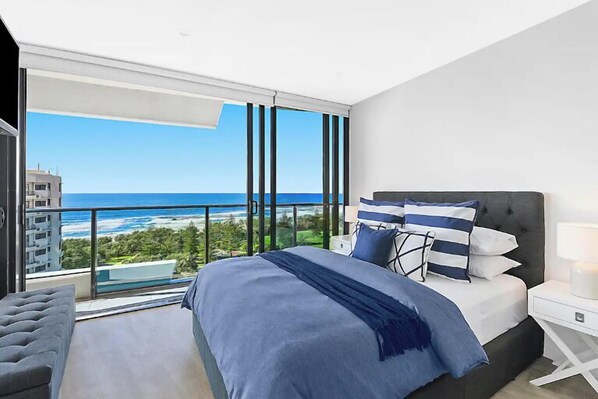 A bedroom with a large bed, a nightstand, a chair, and a view of the ocean. - Luxe by the Beach at Oracle Level 13 (Gold Coast City)