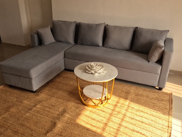 Un canapé modulable assorti d’un pouf, une table basse ronde avec un plateau en marbre et un tapis tissé posé sur un sol carrelé.