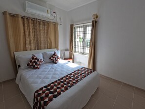 Une chambre avec un lit, une chaise, une fenêtre avec des barreaux et un appareil de climatisation.