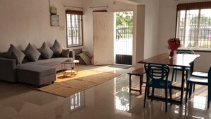 Una sala moderna con un sofá, una mesa de comedor con sillas, una alfombra y una puerta que da al exterior.