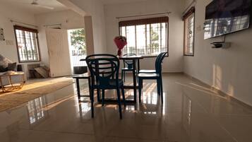 A spacious room with a dining area, a sofa, a TV, and large windows.