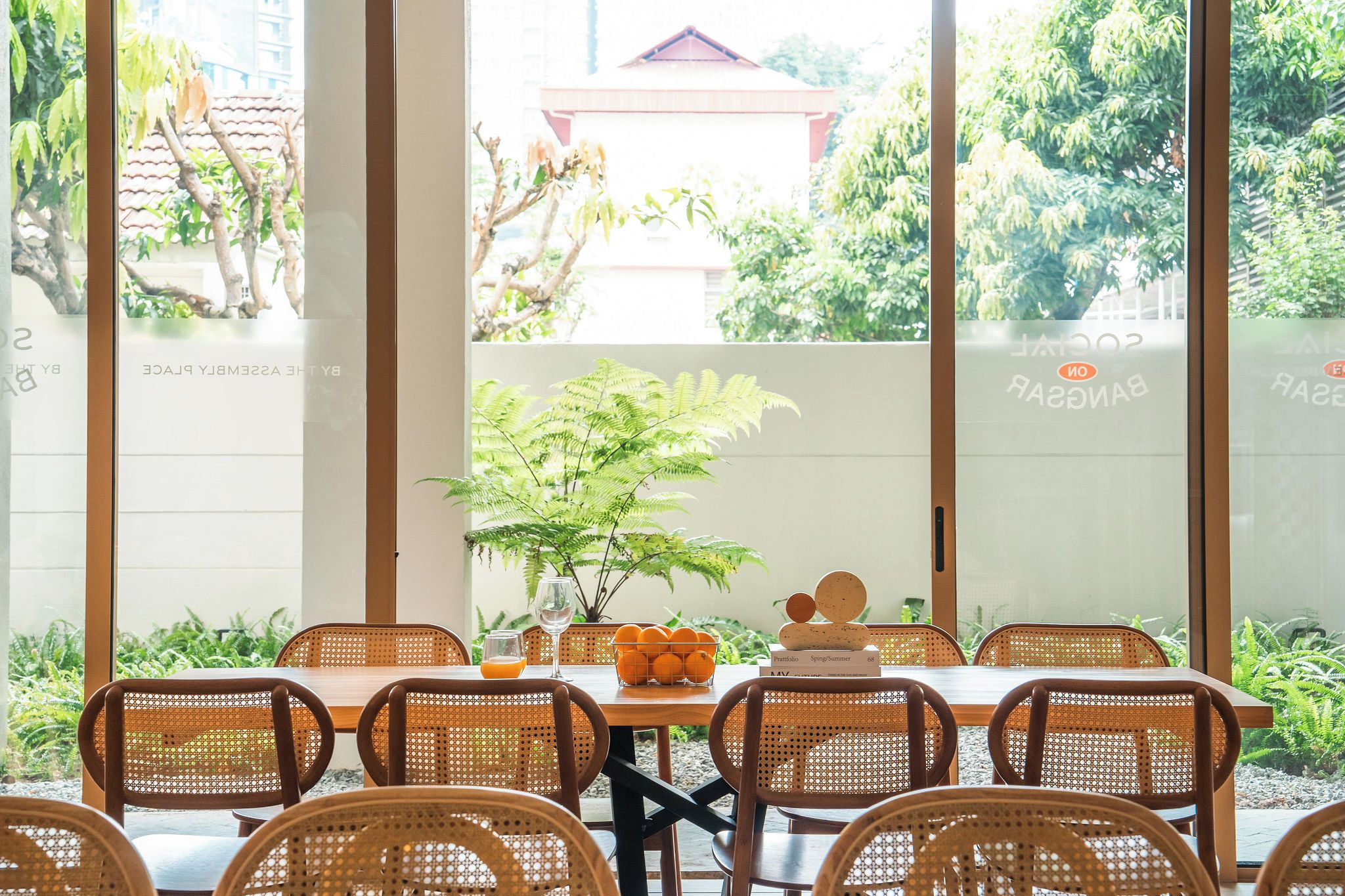 Un comedor con una mesa dispuesta para seis personas, rodeada de sillas de mimbre, con una planta en maceta y un frutero sobre la mesa.