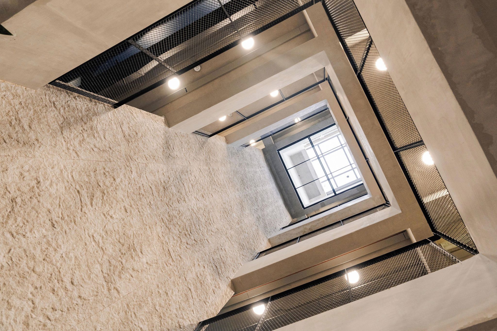 A multi-level interior with a central staircase, a textured floor, and a window allowing natural light.