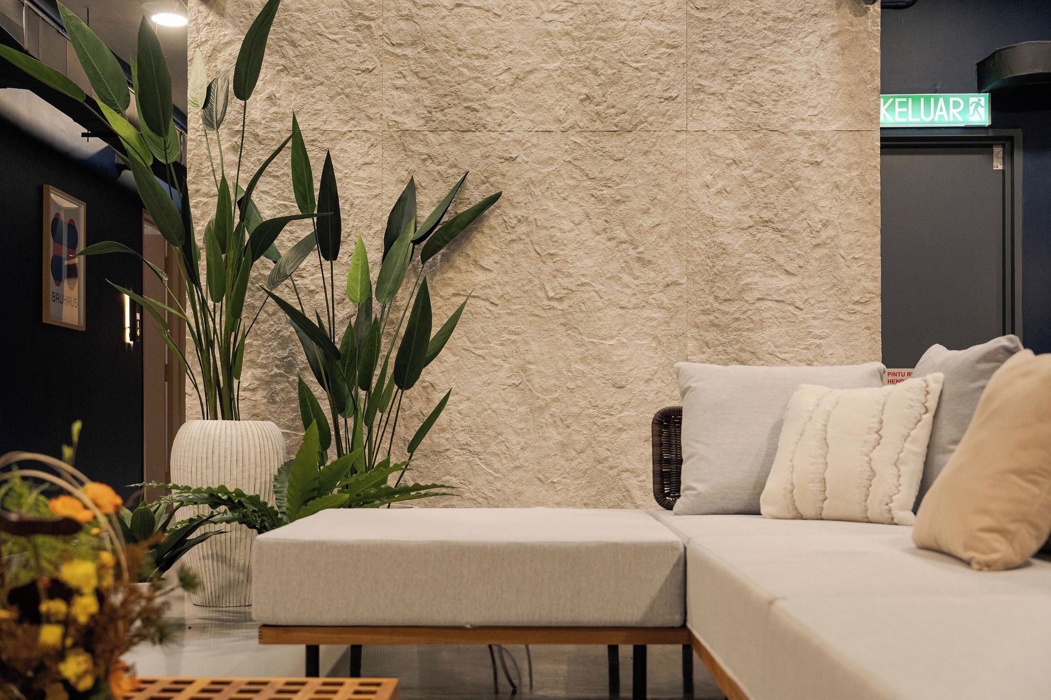 Un interior moderno con una pared con textura, un sofá con cojines y una planta grande.