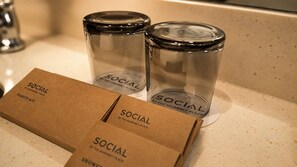 Una caja etiquetada 'SOCIAL BY THE ASSEMBLY PLACE VANITY KIT' y dos recipientes de vidrio transparente con tapas sobre una encimera.
