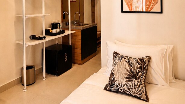 Habitación de hotel con cama, aire acondicionado de pared, cuadro enmarco, armario con espejo y pequeña zona de kitchenette.