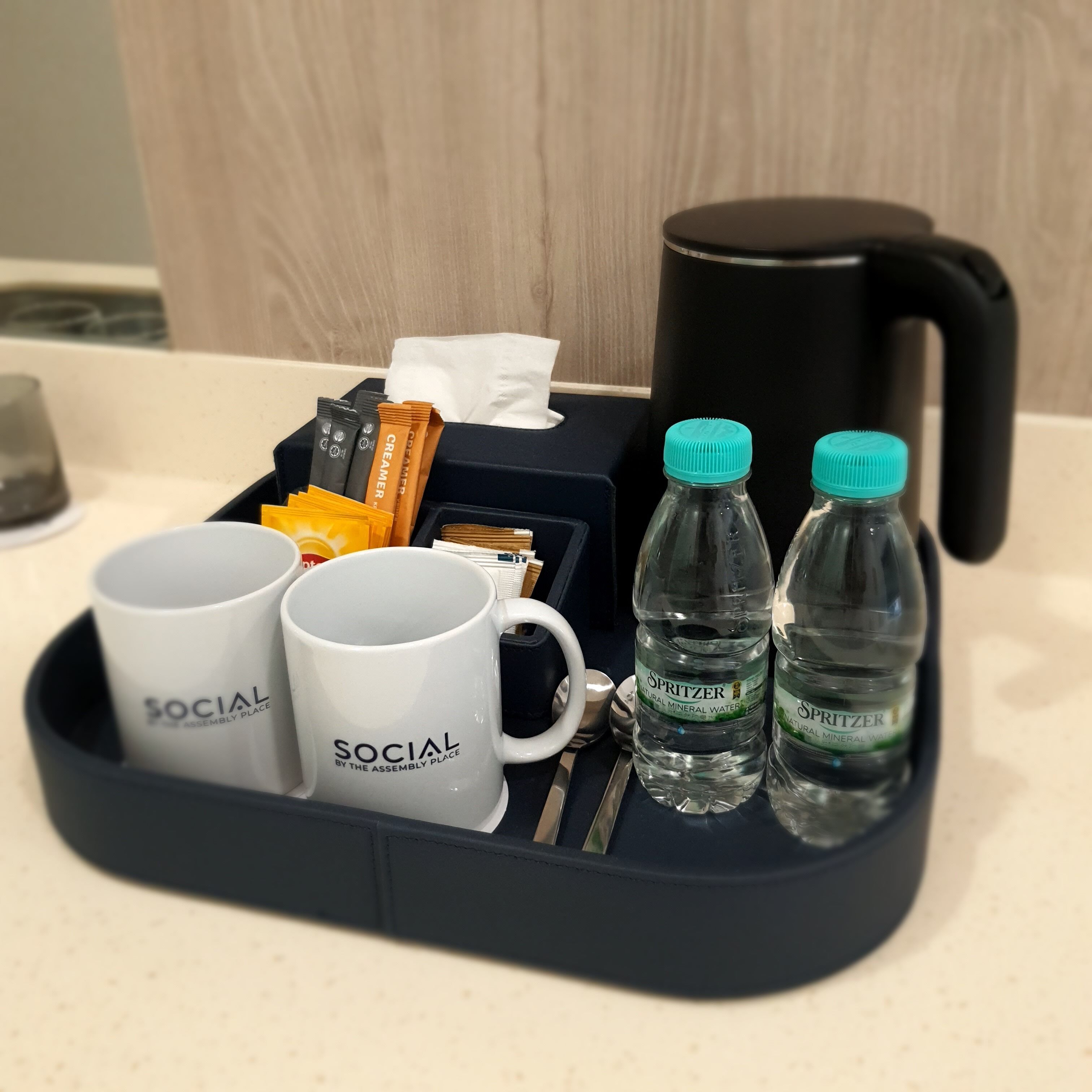 A tray with two white mugs, two bottles of water, a coffee maker, and some snacks.