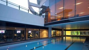 A swimming pool with a glass wall on one side, a second-floor balcony with seating, and a modern architectural design. - Beach Haven at Oracle Level 14 (Gold Coast City)