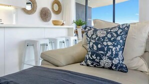 A modern room with a bed, a sofa, a dining area with white chairs, and decorative wall art. - Beach Haven at Oracle Level 14 (Gold Coast City)