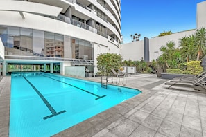 Ein modernes Gebäude mit Swimmingpool, Sitzgelegenheiten im Freien und blauem Himmel.
