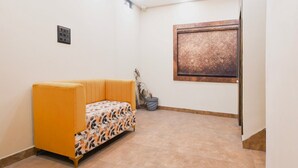 A room with a yellow sofa, a patterned table, a window with a textured design, and a small potted plant. - Hotel O Jamshedpur Near Burma Mines (Golmuri)