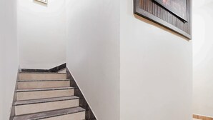A staircase with a handrail, leading to a landing with a framed picture. - Hotel O Jamshedpur Near Burma Mines (Golmuri)