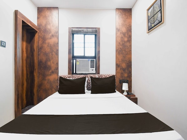 Une chambre à coucher avec un lit, une fenêtre, un climatiseur, une table de chevet et une porte.