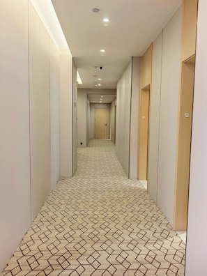 Un couloir avec un tapis à motifs, des spots encastrés au plafond et des portes de part et d’autre.