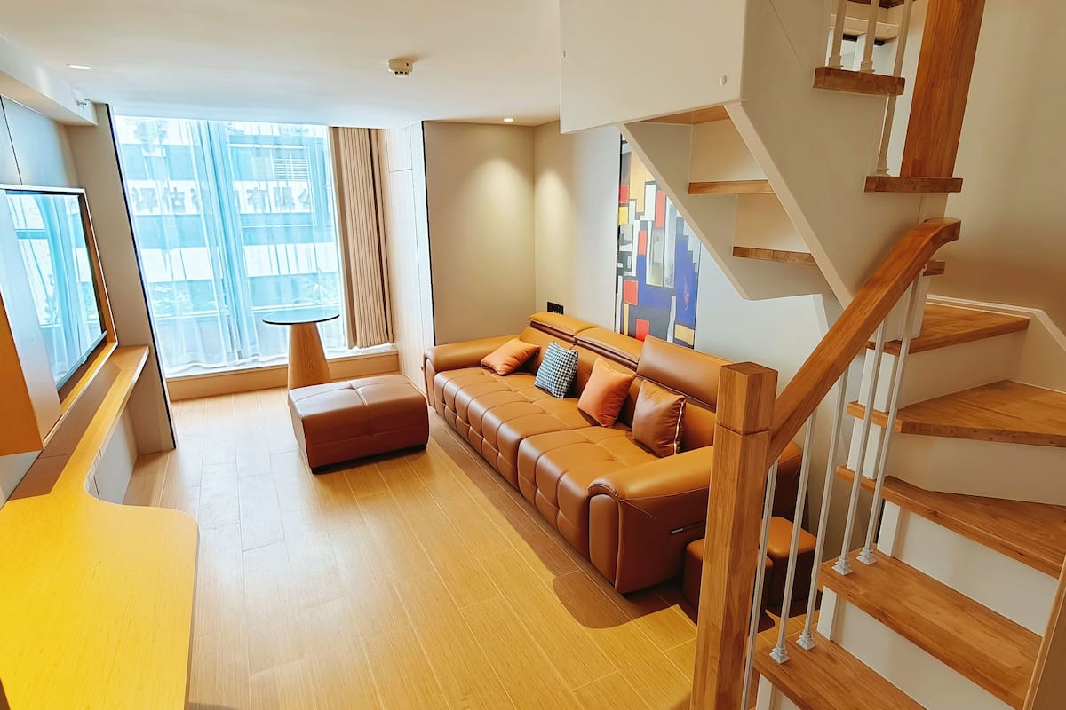 A modern living room with a sofa, ottoman, and a staircase.