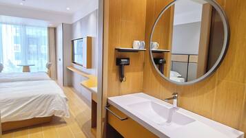 Une chambre d’hôtel avec un lit, une salle de bain comprenant un lavabo et un miroir, et une fenêtre avec des rideaux.