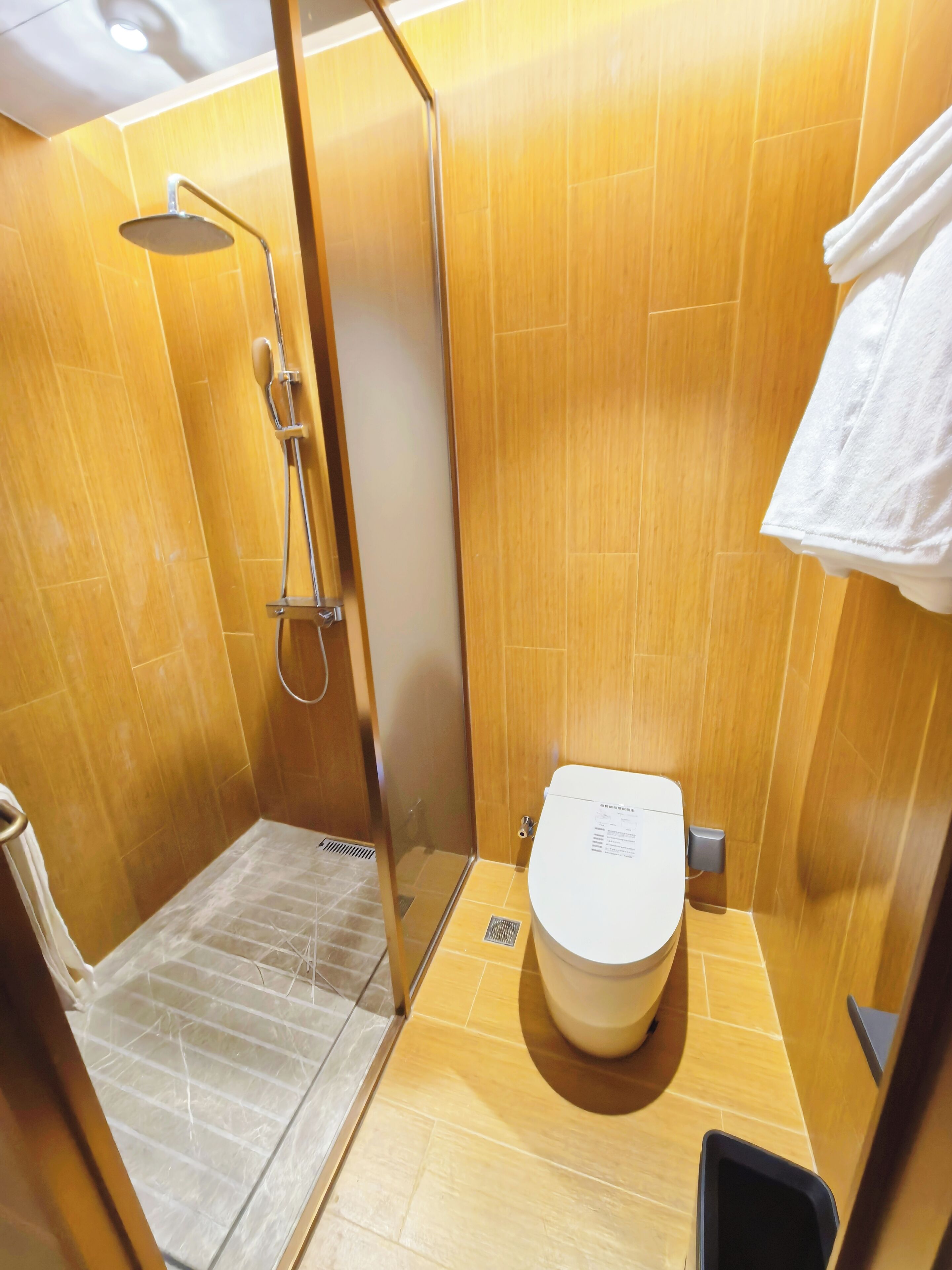 A small, enclosed bathroom with a shower, toilet, and a towel rack.