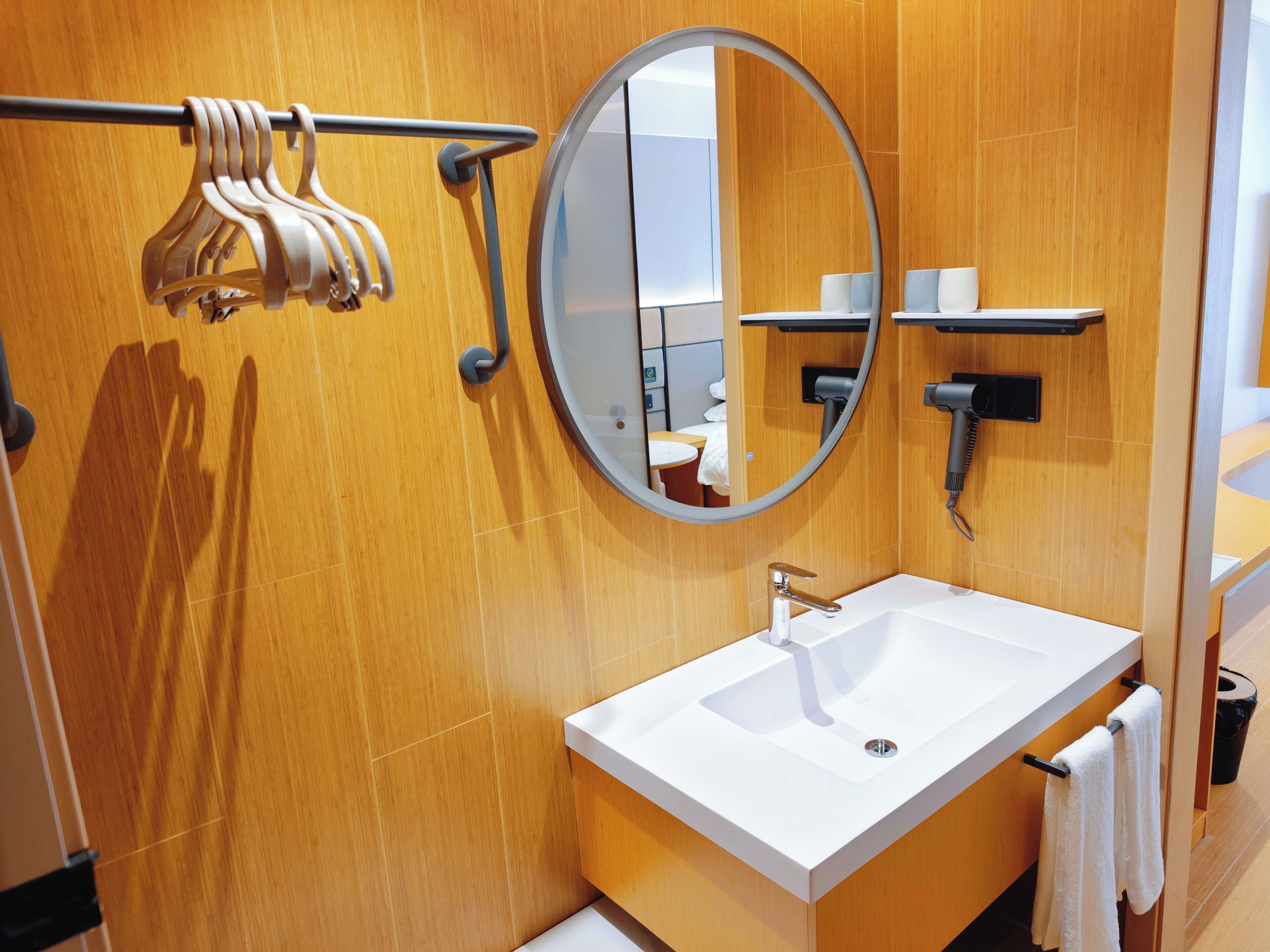 Un baño moderno con tocador de madera, un espejo redondo, un perchero y un secador de pelo.