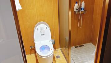 A modern bathroom with a white toilet, a glass-enclosed shower, and a wooden floor.