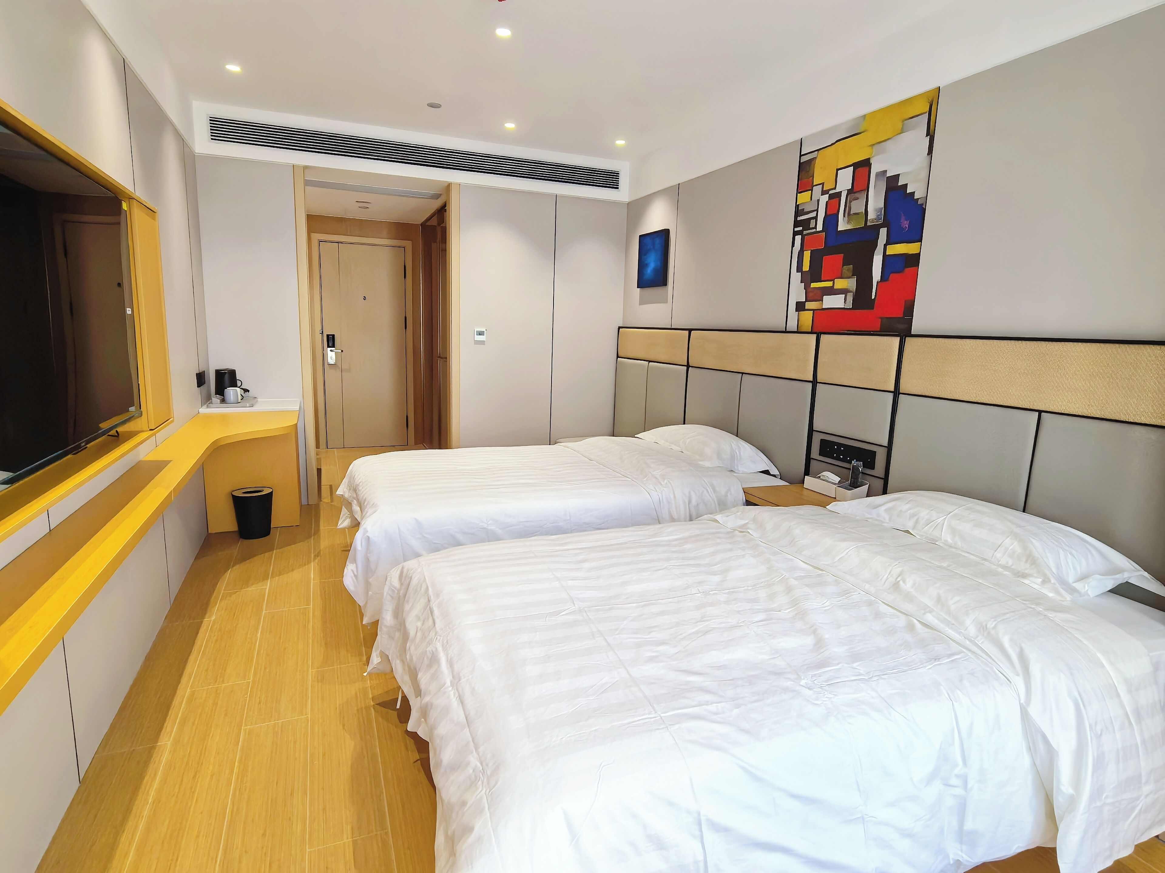 A hotel room with two beds, a TV, a coffee machine, and a painting on the wall.