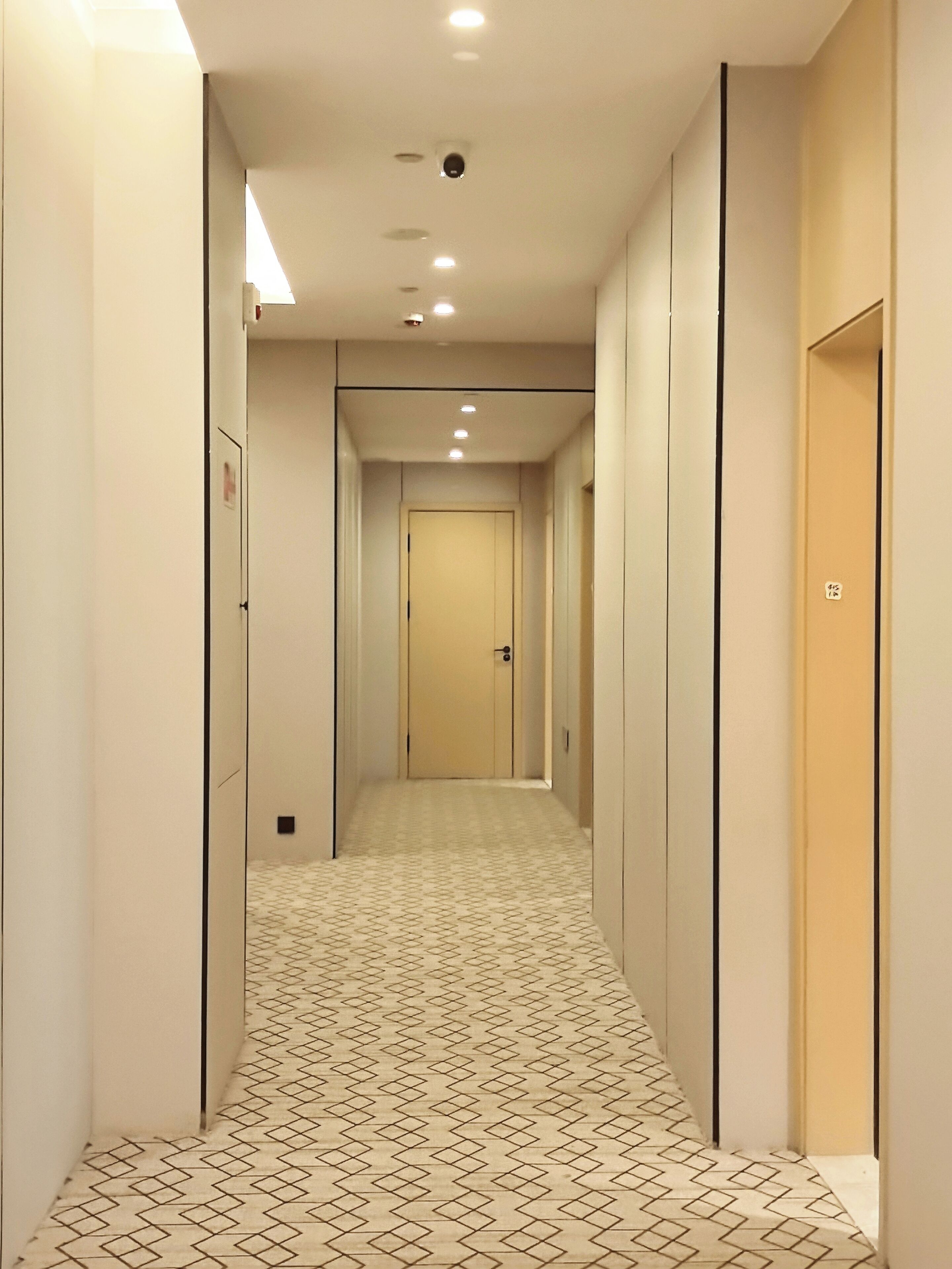 Un couloir d ’hôtel avec un revêtement de sol à motifs, des portes des deux côtés et un éclairage encastré.
