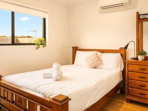 Een slaapkamer met een houten bed, een nachtkastje met een lamp, een dressoir en een raam met uitzicht.