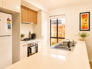 A modern kitchen with a built-in oven, a stainless steel sink, and a window with a view of a wooden deck. - Spacious 4B Near Logan with Parking (Logan Reserve)