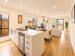 A modern kitchen with a central island, dining area, and a living space with a sofa. - Spacious 4B Near Logan with Parking (Logan Reserve)