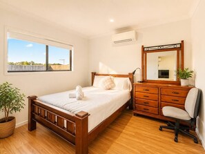 A bedroom with a wooden bed, a dresser, a chair, a potted plant, and a large window. - Spacious 4B Near Logan with Parking (Logan Reserve)