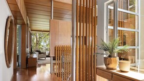 Un interior moderno con suelo de madera, un sofá, una mesa de comedor con plantas en macetas y un ventanal grande.