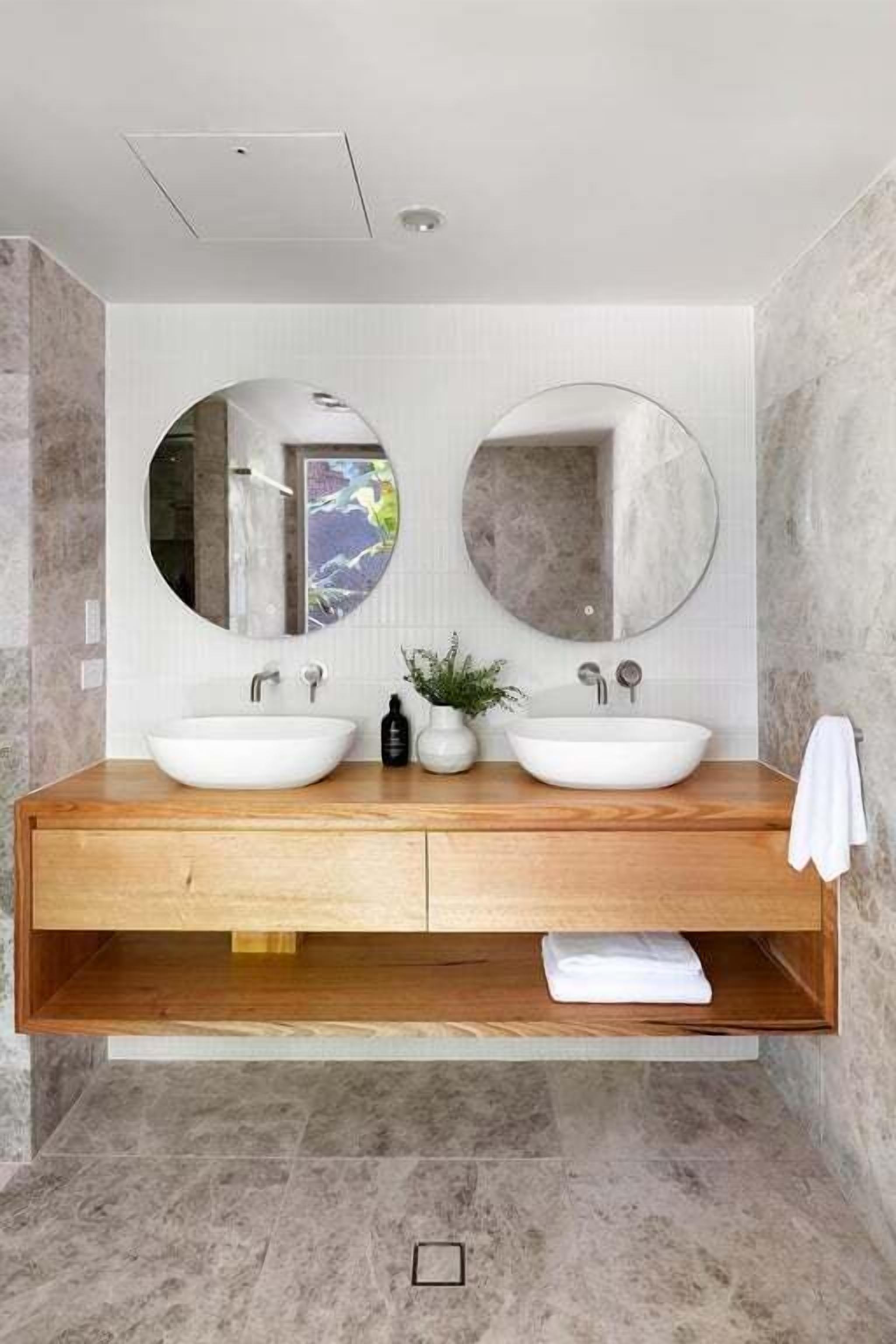 A modern bathroom with two sinks, a wooden vanity, and a large mirror.