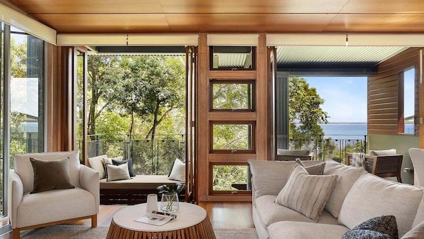 Una sala de estar moderna con un sofá, un sillón, una mesa de centro, ventanas amplias y vista al mar.