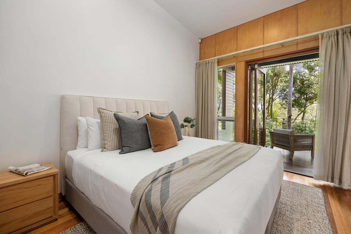 A bedroom with a large bed, a wooden headboard, a nightstand, and a view of the outdoors through a glass door.