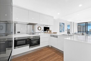 A modern kitchen with white cabinetry, stainless steel appliances, and a wooden floor. - Beach Sunrise at Oracle Level 21 (Gold Coast City)
