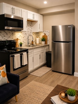 A modern kitchen with white cabinets, stainless steel appliances, a black stove, and a dark blue sofa. - Cozy 1-Bedroom Houston Retreat Near NRG, Downtown & Med Center (Houston)