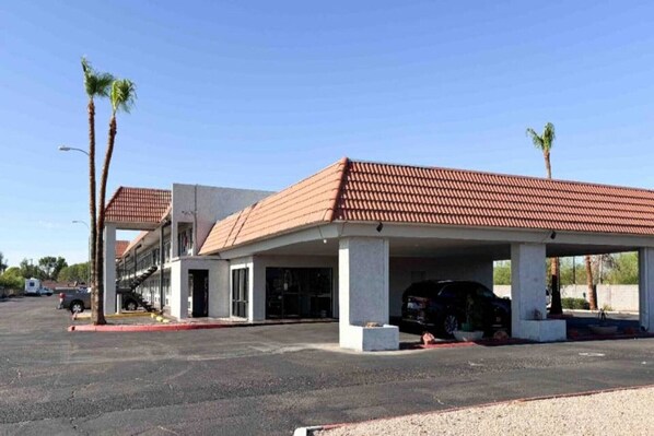 A parking structure with a covered area, a building with a red-tiled roof, and palm trees. - 1 King Bed | Smoking, Micfridge (Mesa)
