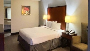 Une chambre d’hôtel avec un lit, deux lampes de chevet, une chaise, un bureau avec un téléphone et un tableau au mur.
