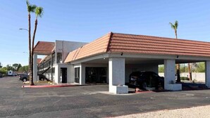 Um edifício de estacionamento com área coberta, um prédio com telhado de telhas vermelhas e palmeiras.